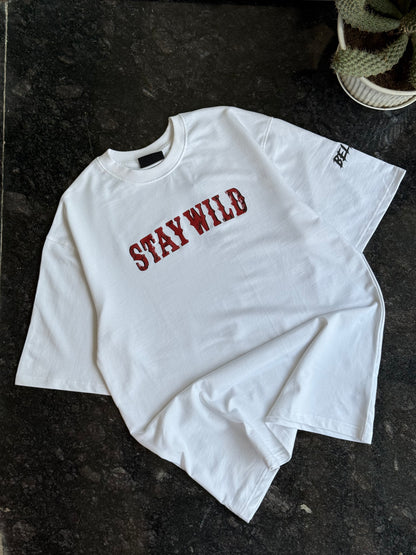 White long-sleeve shirt with 'STAY WILD' text in red on a dark surface.